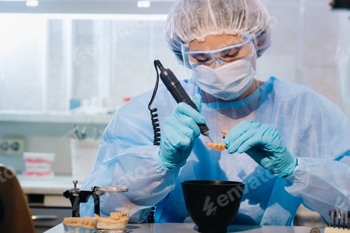 Preview: A dental technician in protective clothing is working on a prosthetic tooth in his laboratory