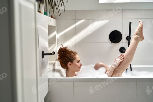 Preview: Young redhead woman taking a bath and holding legs up