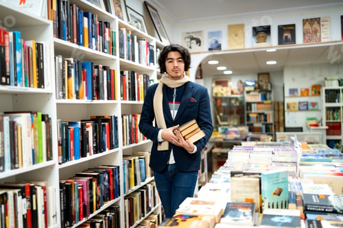 Preview: Young man holding books in a second-hand bookstore aisle
