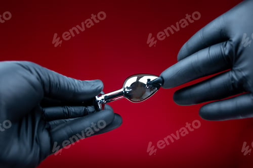 Preview: hands in black gloves holding a silver anal plug for erotic bdsm games