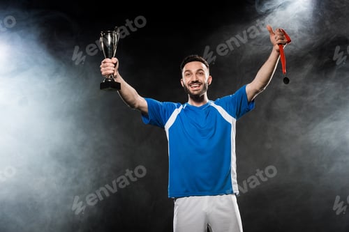 Preview: handsome champion holding trophy and medals in hands on black with smoke