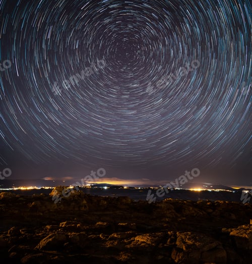 Preview: Town surrounded by lights in the evening under a starry sky with long exposure