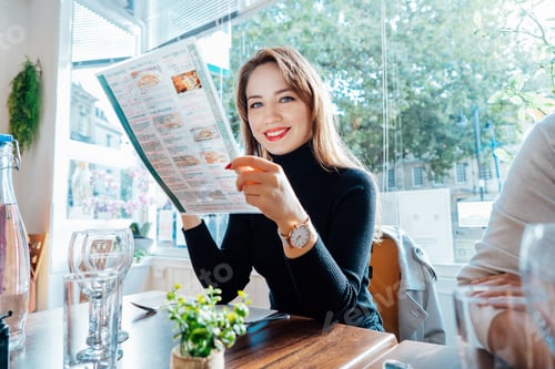 Preview: Young woman reading menu sitting with friend at casual cafe. Smiling woman checking menu,