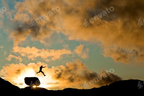 Preview: Silhouette of a person jumping over a rock on a hill during the sunrise in Norway