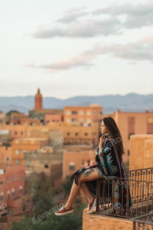 Preview: Woman sitting on roof terrace with aerial view of old arabian town Boumalne