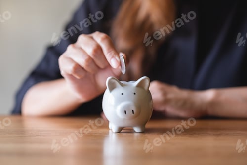 Preview: Closeup image of a woman putting coin into piggy bank for saving money concept