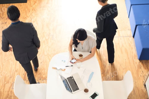 Preview: Overhead view of young businesswoman looking at smartphone at office table