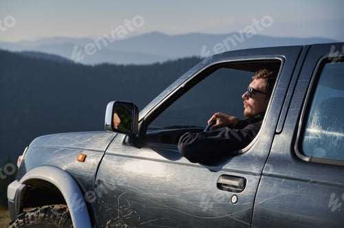 Preview: Man with sunglasses driving black car in the mountains.