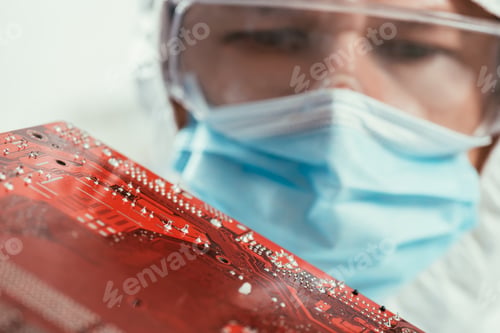 Preview: selective focus of engineer in medical mask and goggles holding computer motherboard