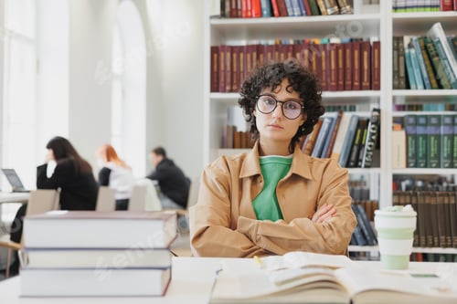 Preview: millennial Spanish woman with wavy hair works at a laptop in a modern library or office