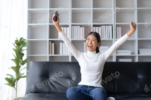 Preview: Asian female reading good news on phone. Surprised asian woman celebrating victory on smartphone
