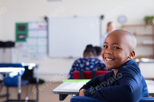Preview: Smiling african american boy sitting at desk in classroom, enjoying school environment