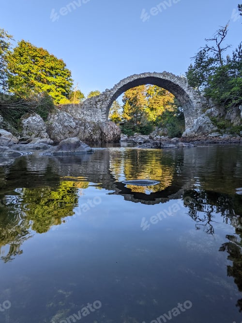 Preview: Vertical shot of the arch bridge reflecting on the river at Carrbridge in Sco