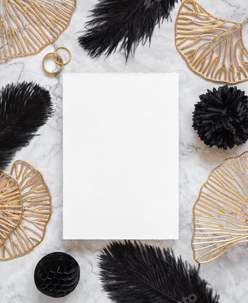 Preview: Blank card on marble table near black feathers and golden leaves with wedding rings top view