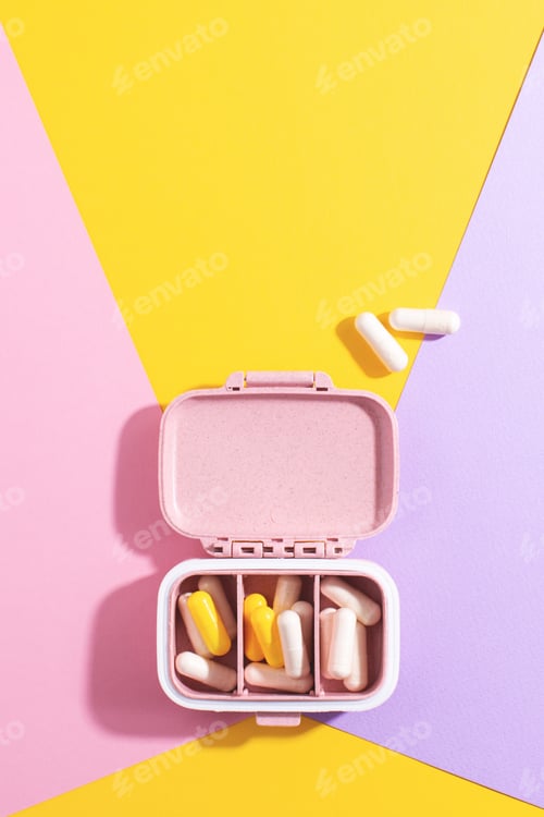 Preview: Open pill box with white and yellow capsules on colourful background.