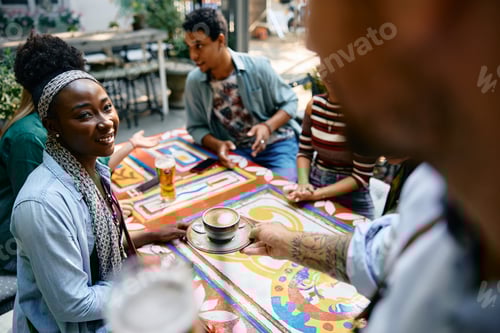 Preview: Happy black woman getting a cup of coffee from a waiter while being with friends in a cafe.