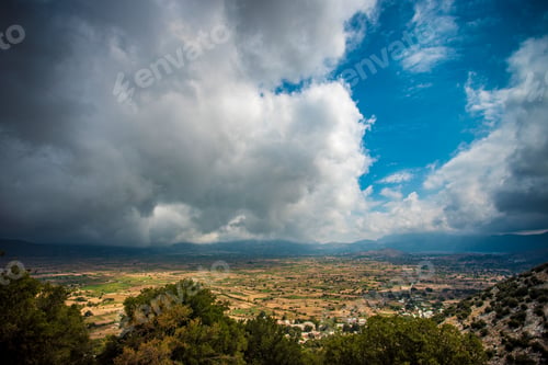 Preview: Cloudy, overcast sky is pictured with lush green trees and bushes in the foreground. Crete, Greece.