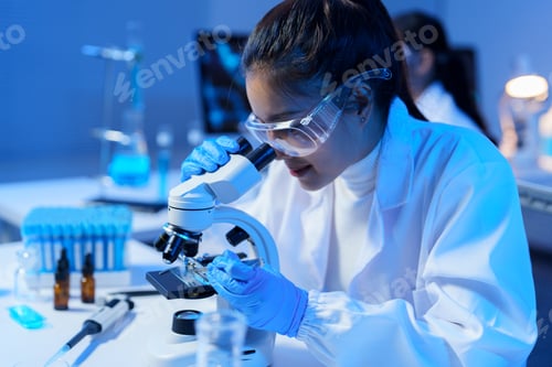 Preview: Scientist wearing a lab coat and safety goggles uses a microscope, carefully examining samples in a