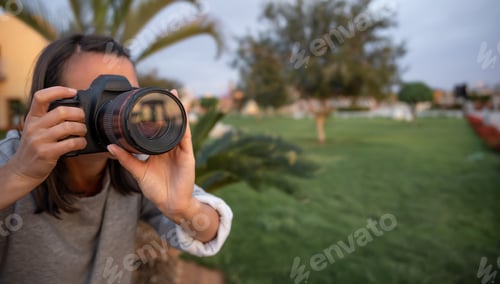 Preview: The girl makes a photo on a professional camera in the garden among the palms.