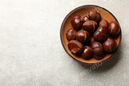 Preview: Fresh edible sweet chestnuts in wooden bowl on grey table, top view. Space for text