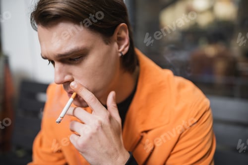 Preview: Young brunette man smoking cigarette outdoors