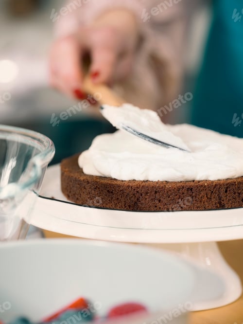 Preview: Cropped view of woman spreading fresh cream on chocolate cake