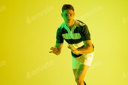 Preview: Caucasian male rugby player catching rugby ball over yellow lighting
