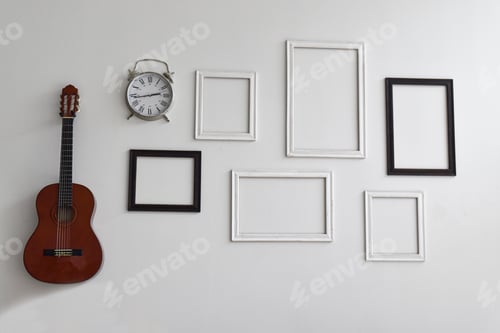 Preview: Blank picture frames, clock and guitar on white cement wall.