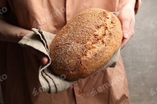 Preview: Woman with loaf of fresh bread against grey background, closeup