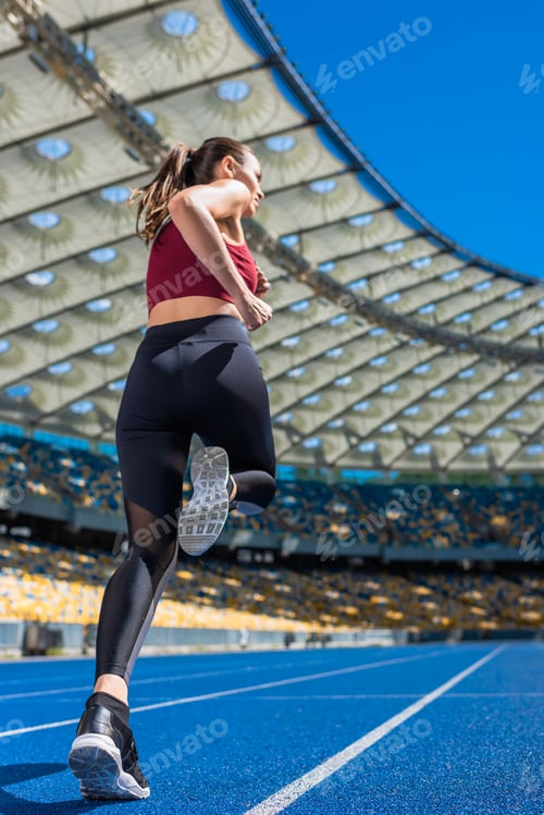 Preview: bottom view of sportive young woman running on track at sports stadium