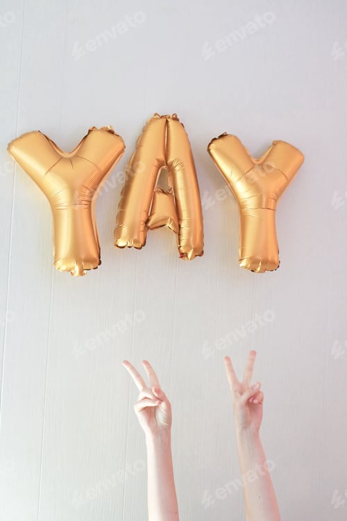 Preview: Golden foil balloons in words YAY. Two hands against the white background. Celebration time.