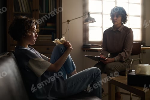 Preview: Young troubled woman sitting on couch in front of psychotherapist