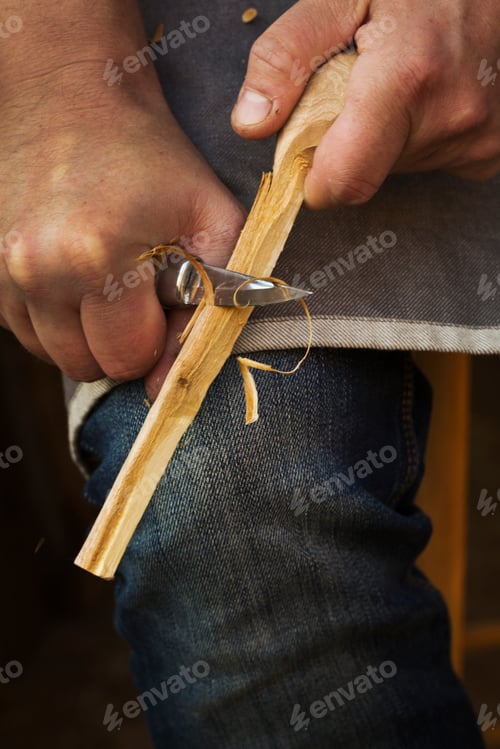 Preview: Close up of a craftsman shaping a small piece of wood with a sharp carving knife.