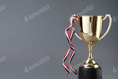 Preview: Golden trophy cup with ribbon on grey background. Space for text
