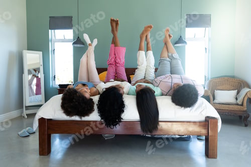Preview: Biracial carefree young biracial friends with feet up lying by side by side on bed against wall