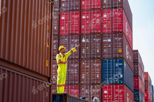 Preview: Worker directs operations at a cargo terminal with stacked shipping containers