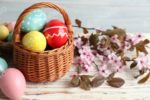 Preview: Painted Easter eggs in wicker basket and blossoming branches on wooden table