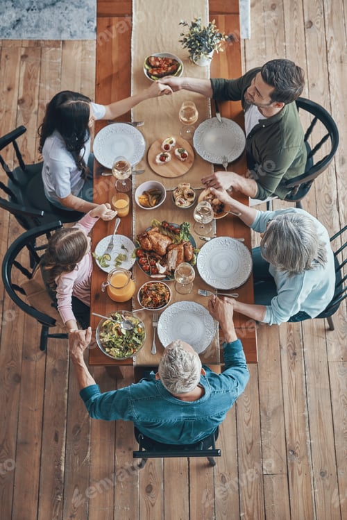 Preview: Top view of multi-generation family holding hands and praying while having dinner together