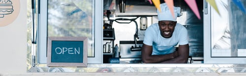 Preview: panoramic shot of happy african american man in chef uniform smiling from food truck