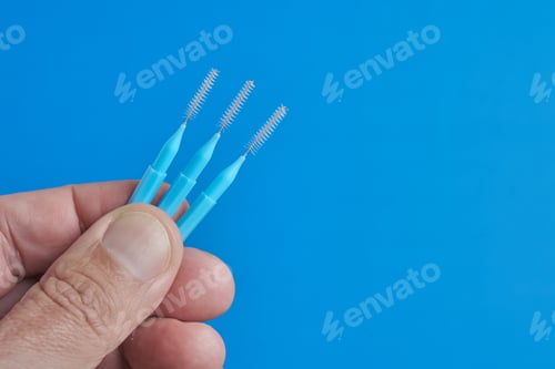 Preview: Hand holding three blue brushes against a bright blue background for cleaning