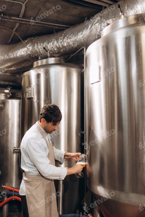Preview: brewer at brewery pours beer into a glass from the tank for inspection