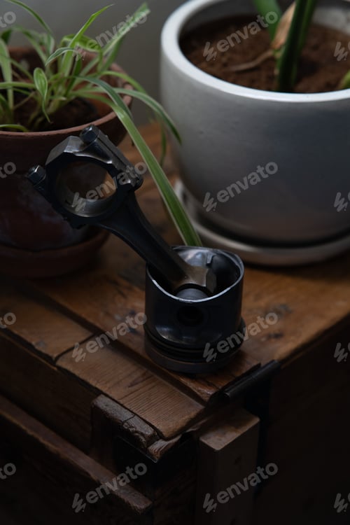 Preview: Car piston and green potted plants on a wooden table at home