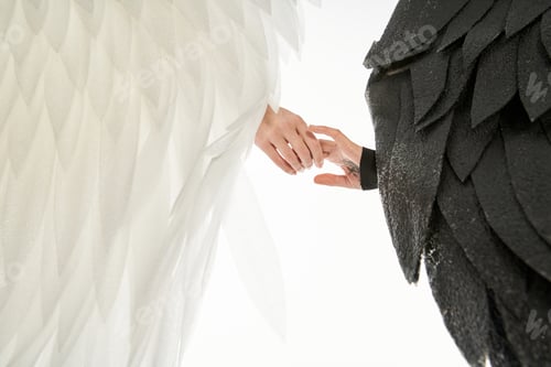 Preview: cropped view of angel and demon with black and light wings holding hands on white