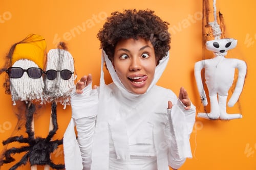 Preview: Funny dark skinned woman sticks out tongue crosses eyes makes funny grimace dressed in ghost costume