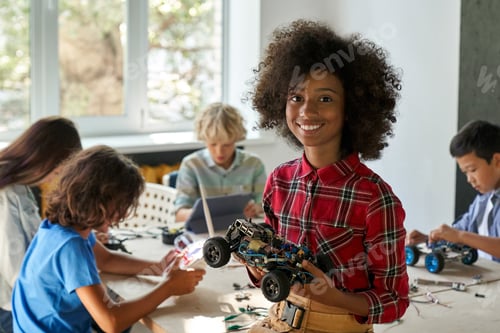 Preview: Happy African American kid school girl holding robotic car at STEM class.