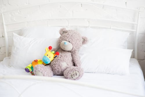 Preview: Two toys: colored giraffe and Teddy bear on a white bed
