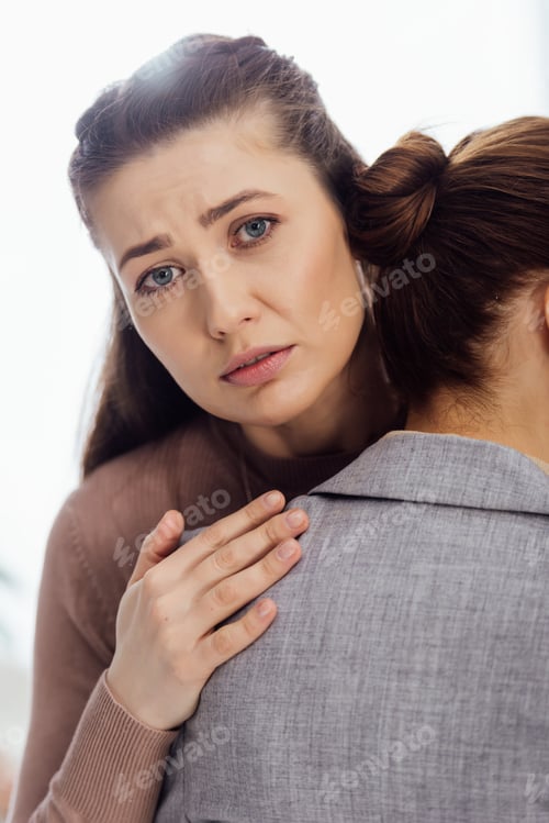 Preview: sad woman looking at camera while embracing another woman during therapy meeting