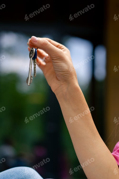 Preview: Woman's hand holding house keys background of cabin in woods A family bought their own new home