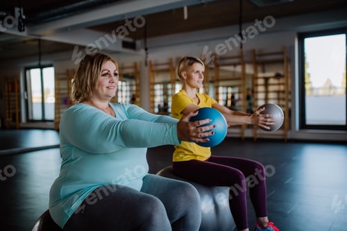 Visualização: Mulher feliz com sobrepeso sentada na bola de ginástica e se exercitando com o personal trainer na academia