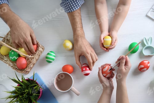 Preview: Father, mother and their child painting Easter eggs on wooden background, top view